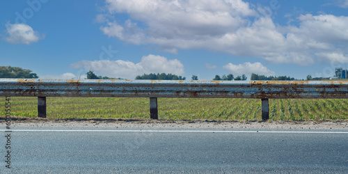 Solid old rusty road safety rail on highway roadside on blue sky background front view