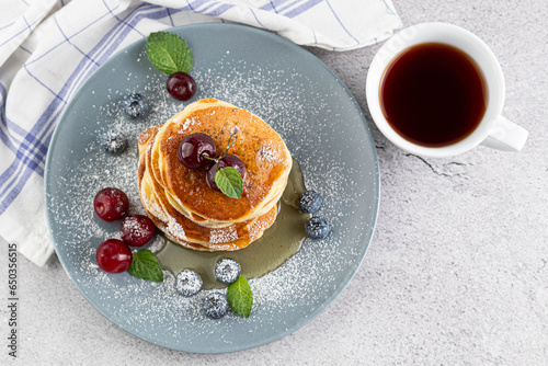 Pancakes with berries in a plate, a cup of tea on a light table. Breakfast concept.
