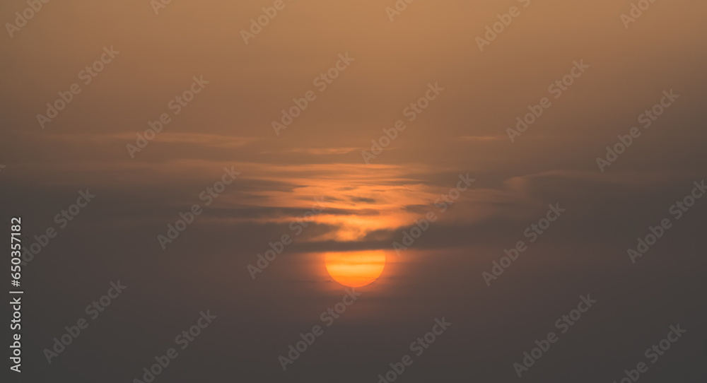 A huge orange sun at sunset highlights the clouds, a minimalistic sunset for the background
