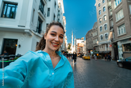 Beautiful young woman smiling and takes selfie at Muslim mosque background while walking along narrow Istanbul street.