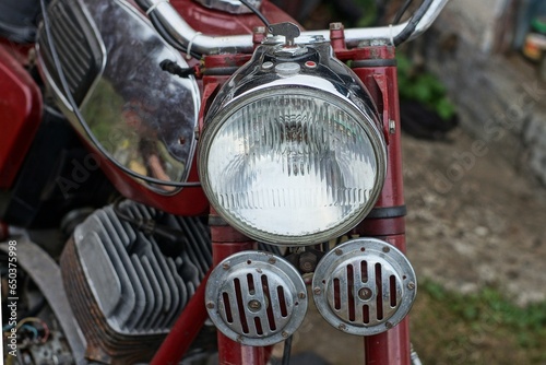 front glass electric round powerful headlight to illuminate the road at night with two iron loud signals iron handlebar and fuel tank of an old heavy classic red motorcycle  on the street