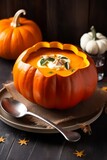 Pumpkin soup with cream, herbs and seeds served in bowl made of pumpkin on the table.
