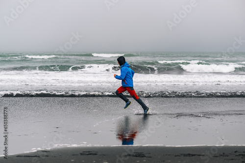 A fit runner in shape is running on the ocean shore in Iceland. There are wild waves in the background.