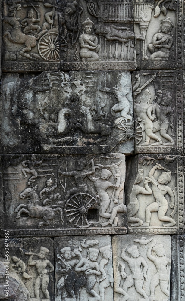 Vertical of stone carvings of Khmer warriors in chariots and war horses in Angkor Wat temple
