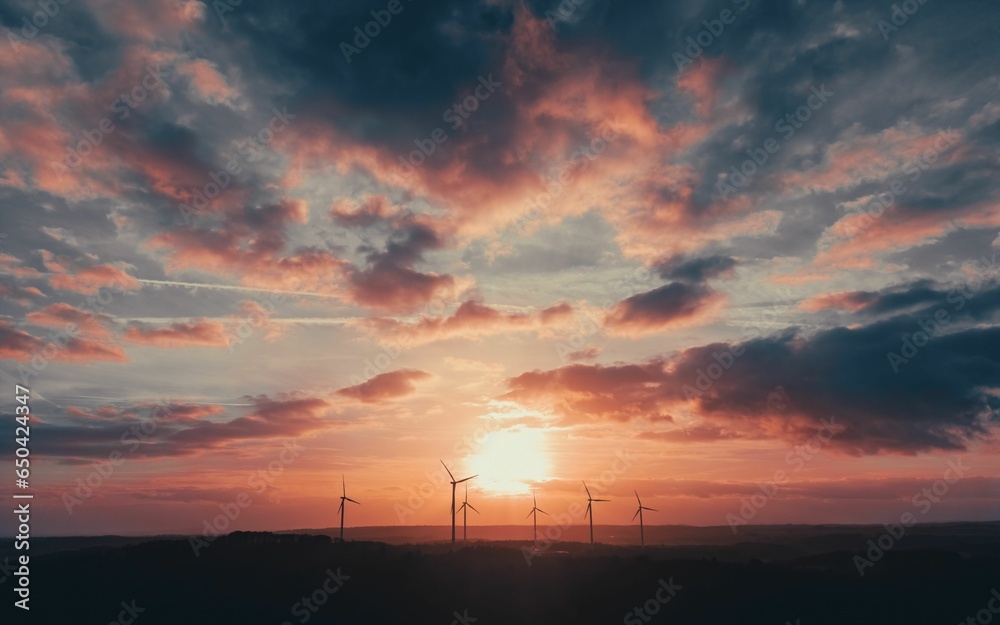 Fototapeta premium Picturesque view of a windmill farm atop a hill with the sun setting in the background