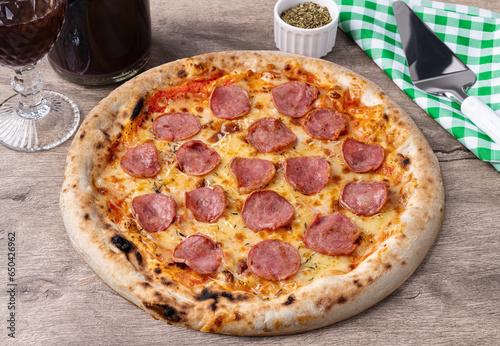 Calabrian sausage style pizza over wooden table with wine, oregano and spatula photo