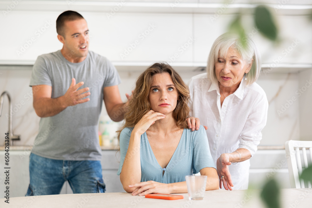 Obraz premium Adult man during family quarrel with elderly woman and adult woman in kitchen