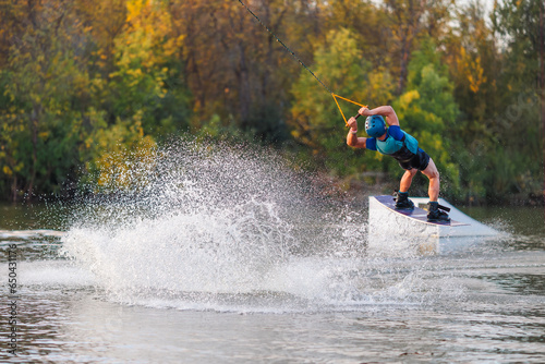 An athlete jumps from a springboard. Wakeboard park at sunset. A man performs a trick on a board