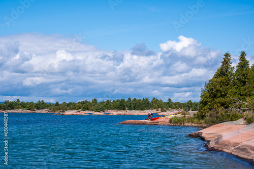 georgian bay dramatic blue sky and white clouds  with scoured rock and green trees in the fore ground where a young man loads a red kayak room for text photo