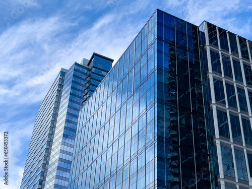 Angled view of a large, window covered building corner against a blue, cloud filled sky