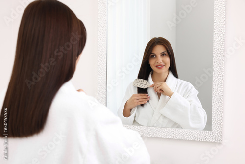 Beautiful woman brushing her hair near mirror indoors