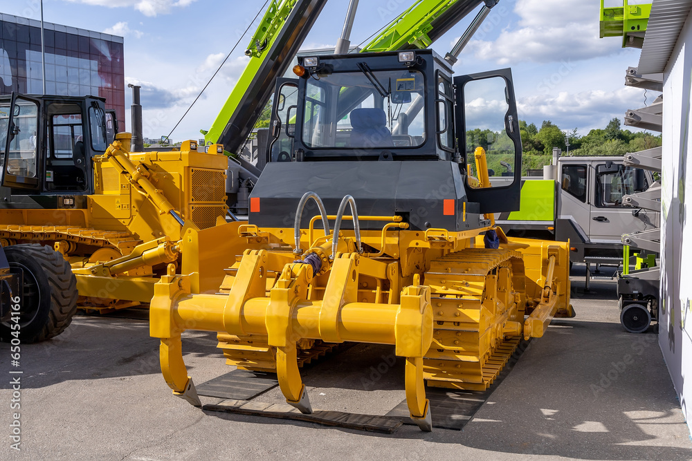 New yellow crawler bulldozer with ripper, rear view. Sale of new construction and municipal equipment at a dealership or fair