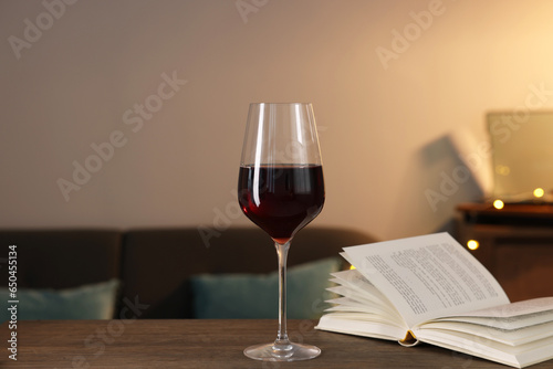 Glass of red wine and open book on wooden table in room. Relax at home