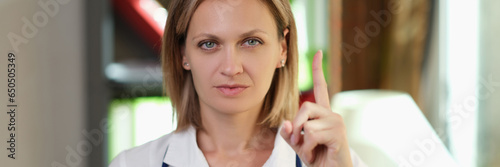 Female doctor with stethoscope shows gesture with her index finger up.