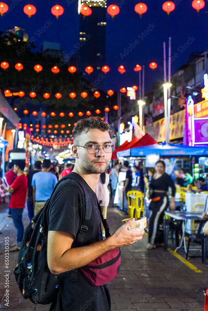 Fototapeta premium Young man tourist eating ice cream in Jalan Alor street food in Kuala Lumpur, Malaysia