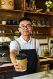 Vietnamese smiling waiter holding paper cups with coffee in a cafe