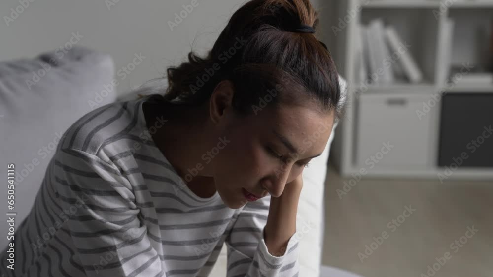 Young Asian woman sitting on sofa at home feeling sad tired and worried suffering depression in mental health. Young Asian woman sitting on sofa at home feeling sad tired and worried suffering depression in mental health.