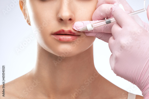 Cosmetologist does injections for lips augmentation and anti wrinkle in the nasolabial folds of a beautiful woman. Women s cosmetology in the beauty salon.