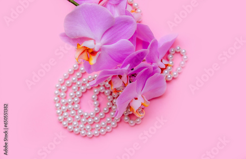 Pearl necklace and purple orchid on pink background 