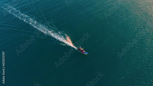 Colorful boat sailing on clean blue Venezuela's sea surface. Aerial drone shot over speed boat with small waves in sea. Concept fast speed boat in clear turquoise magical sea from above in Venezuela.