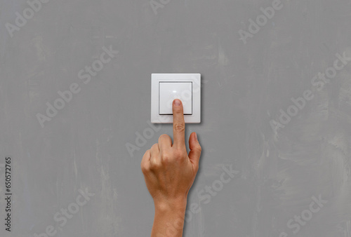 Female finger on light switch close-up on grey concrete wall background. photo