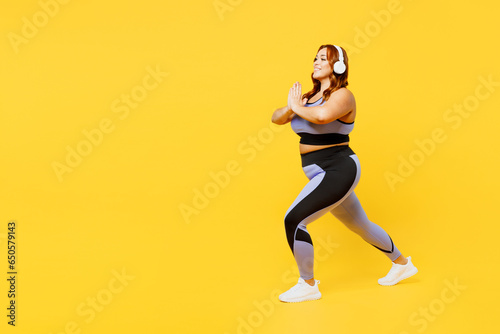 Full body side view young plus size big fat fit woman wear blue top warm up training listen to music in headphones do squates isolated on plain yellow background studio home gym Workout sport concept