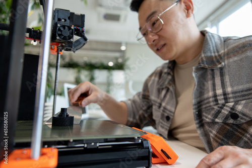 Asian designer engineer using 3D printer in laboratory and studying product prototype.