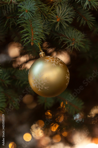 Close up of golden ball on christmas tree. Bokeh garlands in the background. New Year concept. Festive baubles and branch of spruce tree decorated with lights. New Year's Eve. Vintage greeting card.