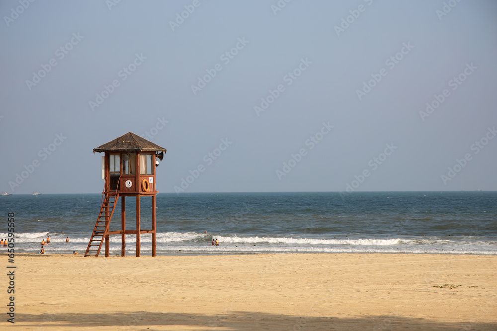 Fototapeta premium lifeguard tower on a hot sunny sandy beach with swimmers in the sea on Hainan Island China with pale blue sky and turquoise sea with breakers and surf a perfect holiday destination for relaxation