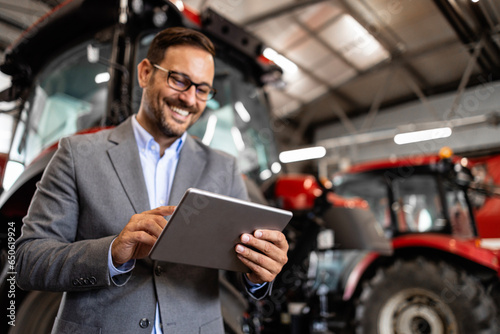Tractor dealer standing in workshop preparing agricultural machines for sale.