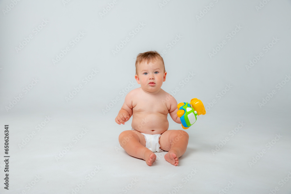 Portrait of a little toddler boy, a baby in a diaper happily sitting playing with a toy car isolated on a white studio background. The concept of childhood, motherhood, life, birth. Place for text Portrait of a little toddler boy, a baby in a diaper happily sitting playing with a toy car isolated on a white studio background. The concept of childhood, motherhood, life, birth. Place for text