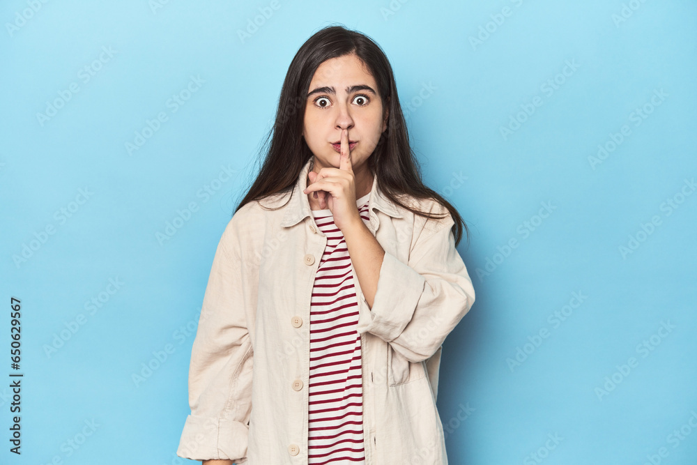 Young Caucasian woman on blue backdrop keeping a secret or asking for silence. Young Caucasian woman on blue backdrop keeping a secret or asking for silence.