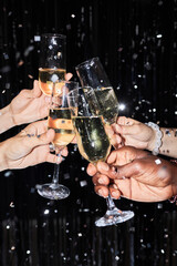 Closeup of group of friends toasting with champagne glasses at party against glittering background with confetti