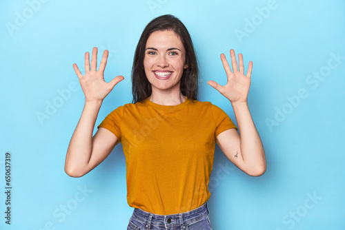 Young caucasian woman on blue backdrop showing number ten with hands.