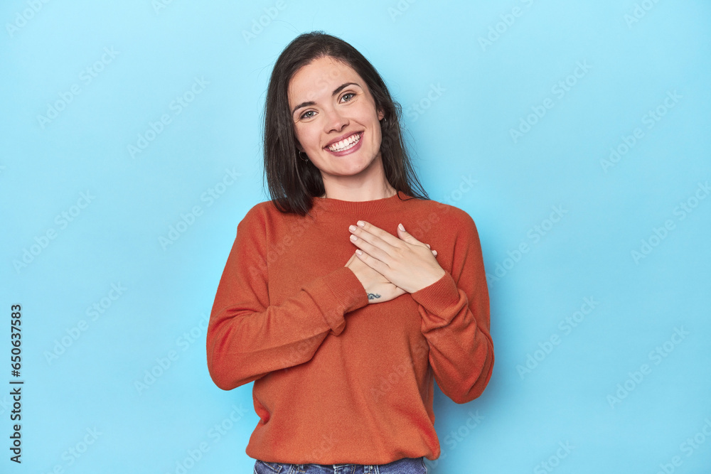 Young caucasian woman on blue backdrop has friendly expression, pressing palm to chest. Love concept. Young caucasian woman on blue backdrop has friendly expression, pressing palm to chest. Love concept.