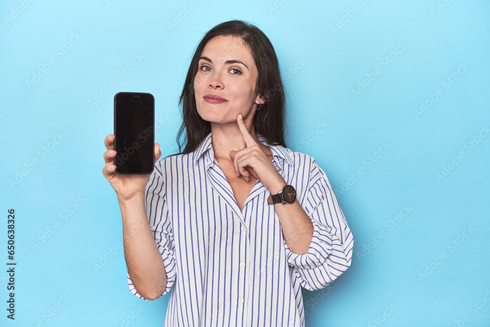 Woman displaying phone screen on blue backdrop Woman displaying phone screen on blue backdrop