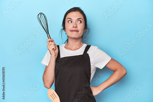 Chef in apron holding manual whisk, ready to mix on blue