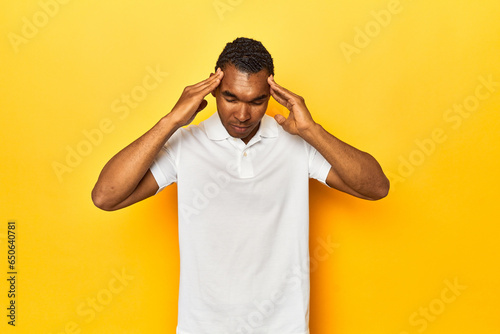 African American man in white polo, yellow studio, touching temples and having headache.