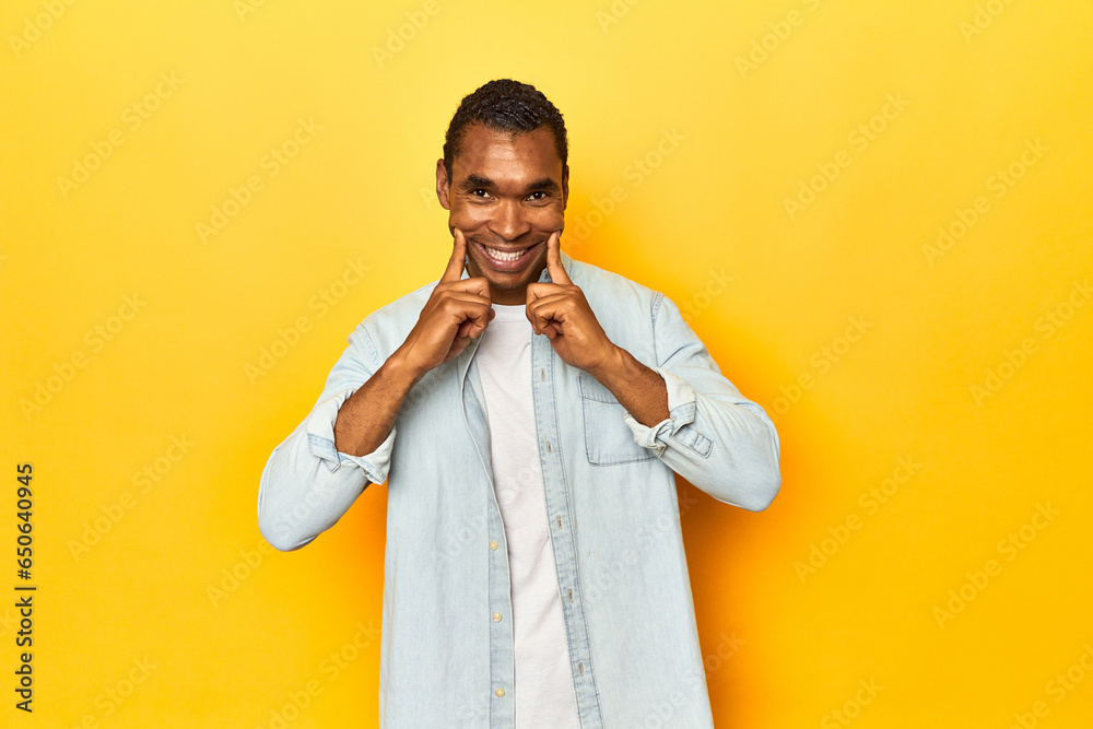 African American man in blue shirt, yellow studio, doubting between two options.