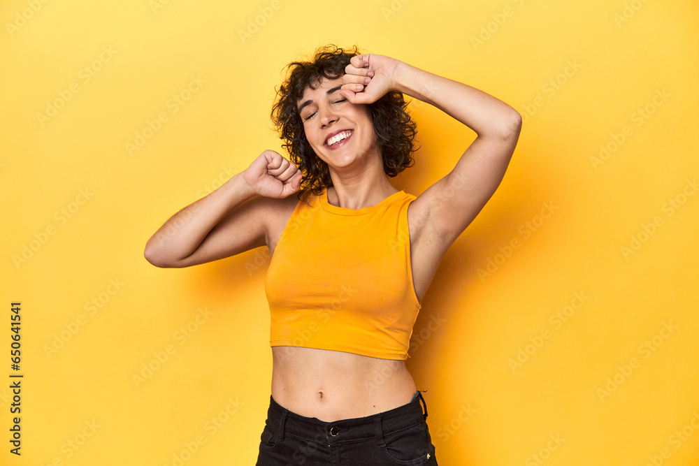 Curly-haired Caucasian woman in yellow top celebrating a special day, jumps and raise arms with energy. Curly-haired Caucasian woman in yellow top celebrating a special day, jumps and raise arms with energy.