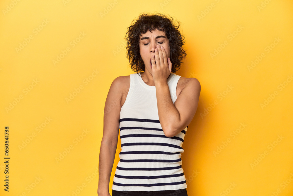 Caucasian curly-haired woman in white tank-top yawning showing a tired gesture covering mouth with hand. Caucasian curly-haired woman in white tank-top yawning showing a tired gesture covering mouth with hand.