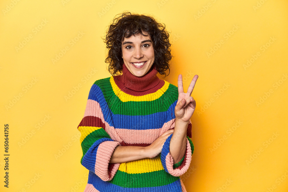 Curly-haired woman in multicolor sweatshirt showing number two with fingers. Curly-haired woman in multicolor sweatshirt showing number two with fingers.