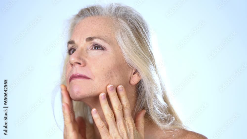 Closeup of mature middle aged woman looking at her face and neck skin wrinkles and smiling isolated on white background with copy space.