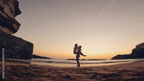 One happy and cute woman running to her boyfriend in love at sunset on the sand of the beach. Happy couple of millennials teenagers enjoying together. Young man holding girlfriend on his arms photo