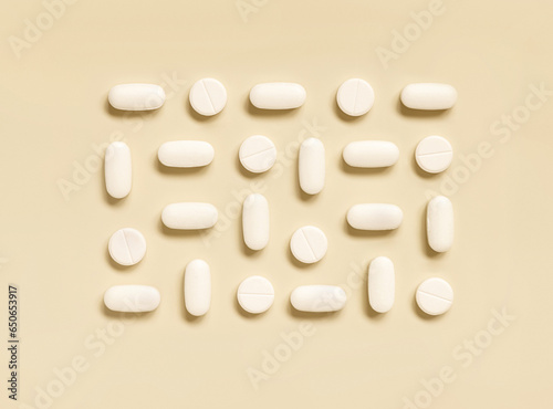 Mix of white medical pills in a line on light beige top view. Dietary supplements