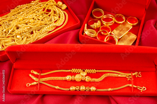 The Many gold necklaces and gold bars in red box on red velvet cloth background.