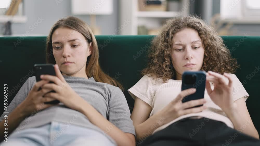Phone addiction of young women looking at smartphone screen during the day while sitting on couch, looking tired ignore each other