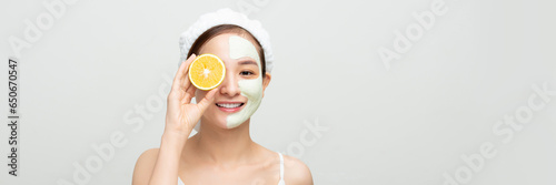 Smiling woman with orange slice and mud mask on face for web banner