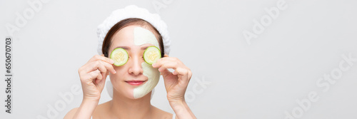 Woman with facial mask holds sliced cucumber, over white banner background