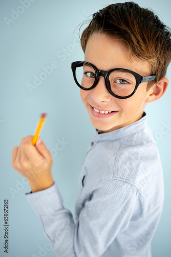 cool, cute young schoolboy with blue shirt, black glasses and pencil in front of blue background